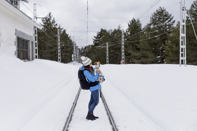年轻女子走在雪山和铁路旁。可爱的小狗和她的主人散步。活跃的女性在户外