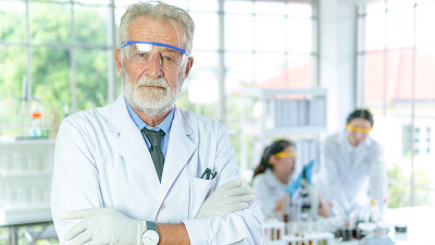 英俊的资深科学家男子穿着白色大褂站在室内实验室背景前微笑着积极。成功的面孔和情感的表达。