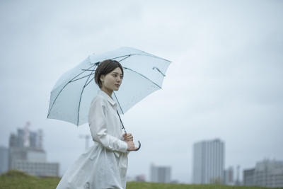 一个穿着白色连衣裙的年轻女子撑着伞在雨中行走