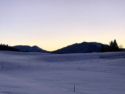 在一个晴朗的冬日，瑞士施维茨州雪景上的日落。地面上有金属杆，标明雪的深度。地平线上是小山，背景是柔和