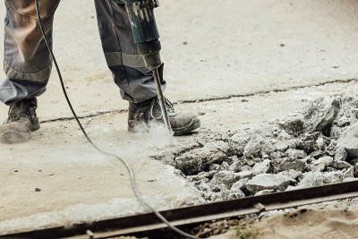 一个工人在夏天用手提钻修理路面。道路上的建筑工程