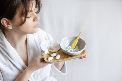 一个穿着长袍的年轻女子拿着一个装有粘土面膜的碗。