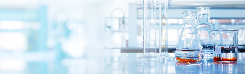水和橙色溶液在玻璃烧瓶和圆筒在柔和的蓝色光医学科学实验室横幅背景