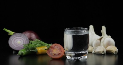 用小酒杯喝伏特加。背景用蔬菜