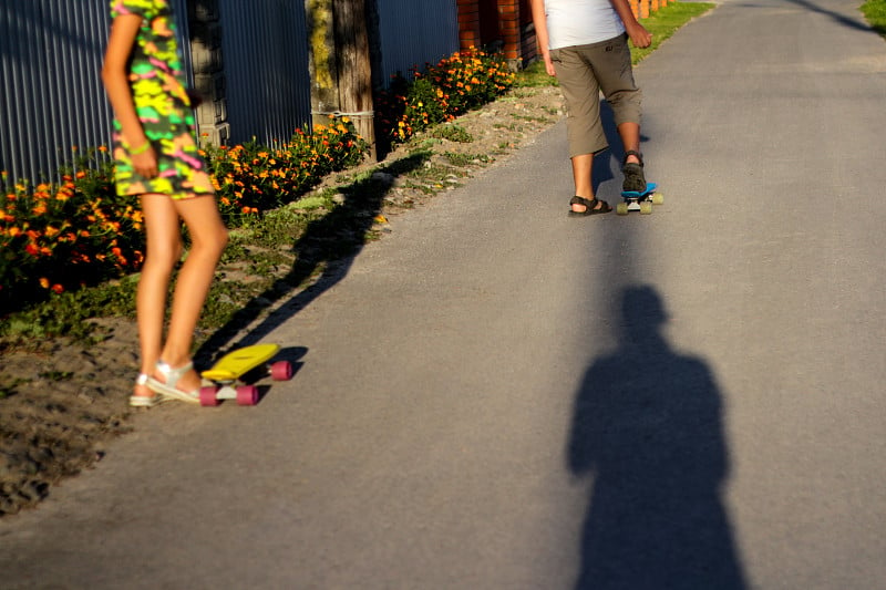 离焦与便士滑板在道路上的公园小孩。男孩和女孩在阳光明媚的日子里玩硬币板。户外生活方式图片在一个阳光明