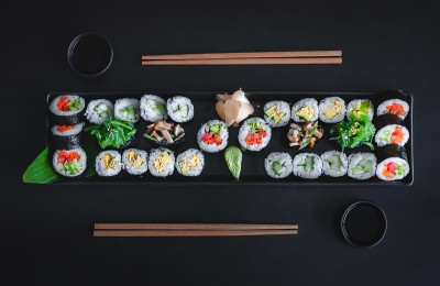 素食寿司套餐包括蔬菜卷、牛油果卷、海带和蘑菇卷，配酱油、芥末和腌姜。俯视图，黑色背景。