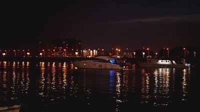 豪华的现代私人游艇和游艇在晚上的码头。夜晚，城市的彩灯在水波中闪烁。