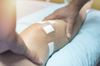 在医院病床上做韧带手术后，医生触摸病人腿上的手，保健和医疗理念。