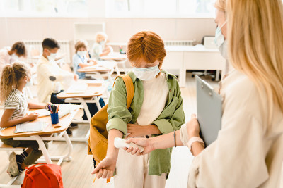 老师在女学生的手腕上测量温度，学生同学在上课前戴着防护药物口罩，以防止因封锁限制新冠肺炎。