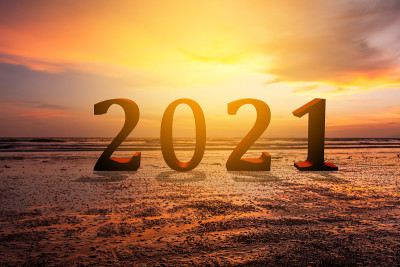 新年概念，在沙滩上模糊的日落天空背景上的2021文字。