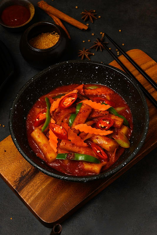 韩式饮食风格:俯视图的热辣炒年糕(Tteokbokki)，放在黑色的碗或盘子，并放在一个木制托盘