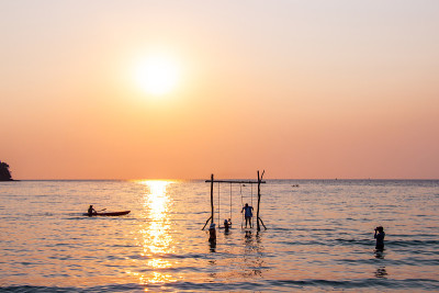 夕阳西下时，游客们在泰国特拉特奥邦宝古岛的海水中嬉戏。