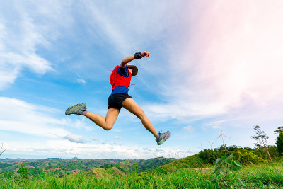身穿运动服的亚洲女选手们正在美丽的风景后面的高山上练习跑、跳。背景中有一个风力涡轮机在发电。