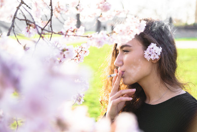 女孩侧身站在户外的树旁抽烟