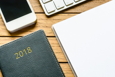 俯视图:一个整洁的木制桌面，上面有2018年的日记、智能手机、键盘和笔记本