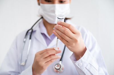 一名戴着口罩的女医生站在实验室里，手里拿着装有防护新型冠状病毒疫苗的注射器。预防COVID-19传播