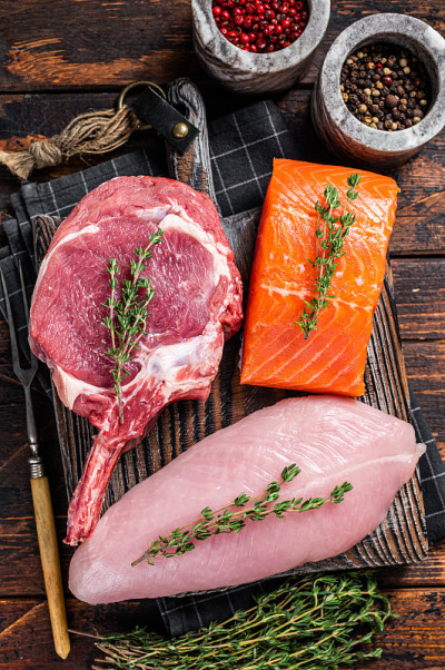 生牛排-鱼鲑鱼，牛肉和火鸡胸脯肉在砧板上。木制背景。俯视图