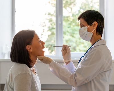戴防护口罩的中年医生检查病人的喉咙和口腔