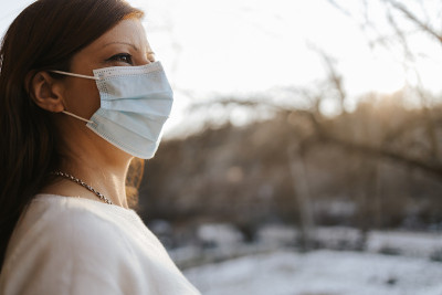 年轻女子在家的露台上戴着防护口罩，享受阳光明媚的冬日