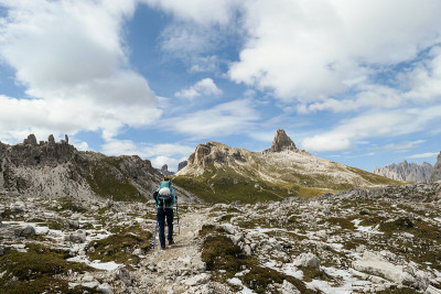 一名女子背着背包，拄着拐杖在意大利Dolomites的一条狭窄小路上徒步旅行。那里有陡峭的山。在一个