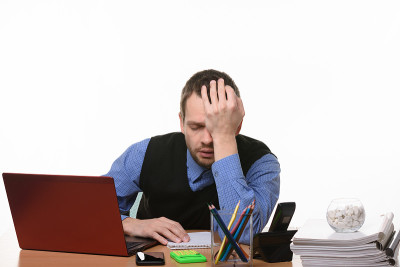 一个疲惫不堪的办公室职员坐在桌边，用手托着头休息