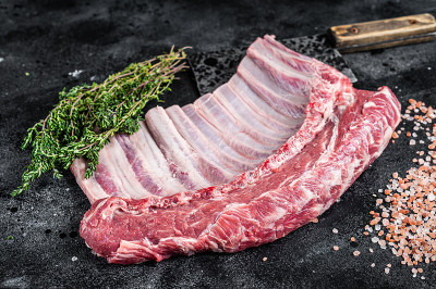 肉切板上的生羊排骨，配香草。黑色背景。俯视图