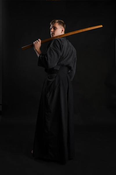 剑道大师穿着传统的日本和服正在练习武术与shinai竹剑在一个黑色的工作室背景