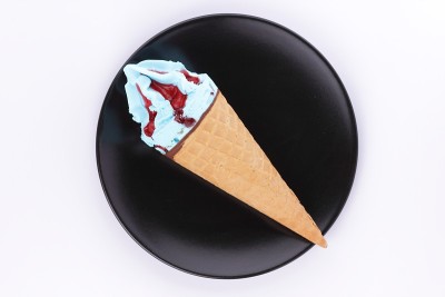 冰淇淋装在一个华夫饼杯里，里面有五颜六色的馅和红色的果酱，放在一个黑色的盘子里，还有一个专门为设计师