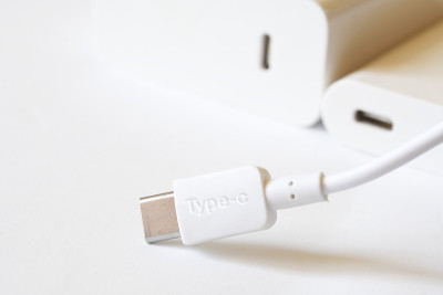 一个带电线的白色usb type-c型连接器靠在明亮的背景下，旁边是两个匹配的白色连接器——一个电源