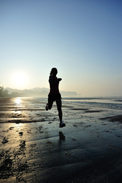 年轻的健身女性在日出的海滩上跑步