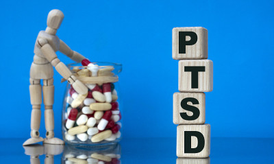 创伤后应激障碍(PTSD)的文本在一个蓝色背景的木块上，药丸和一个木制的人