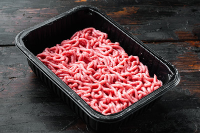 碎牛肉放在塑料托盘里，旧的深色木桌背景上