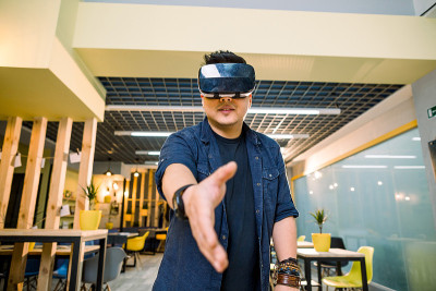 年轻的中国商人戴着虚拟现实眼镜在办公室工作。在增强现实中使用VR头盔握手的人