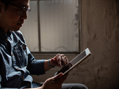 在温暖的阳光下坐在沙发上浏览平板电脑的男人。