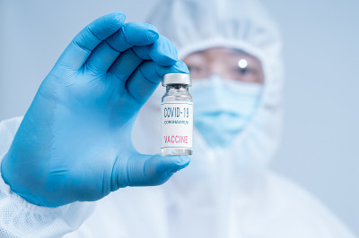 一名男性科学家戴着蓝色手套，穿着防护服，手里拿着Covid-19疫苗。