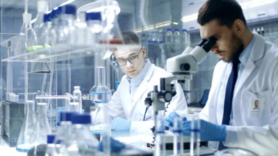 在一个现代实验室里，两位科学家进行实验。首席研究科学家将他在显微镜中看到的结果口述给他的助手。