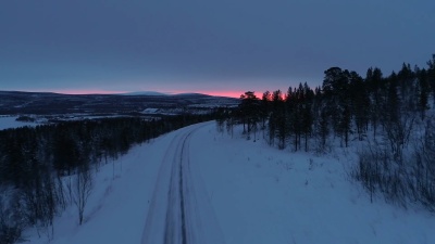 空中 粉红色的日落时分，空旷的雪山公路穿过冬日的云杉林。