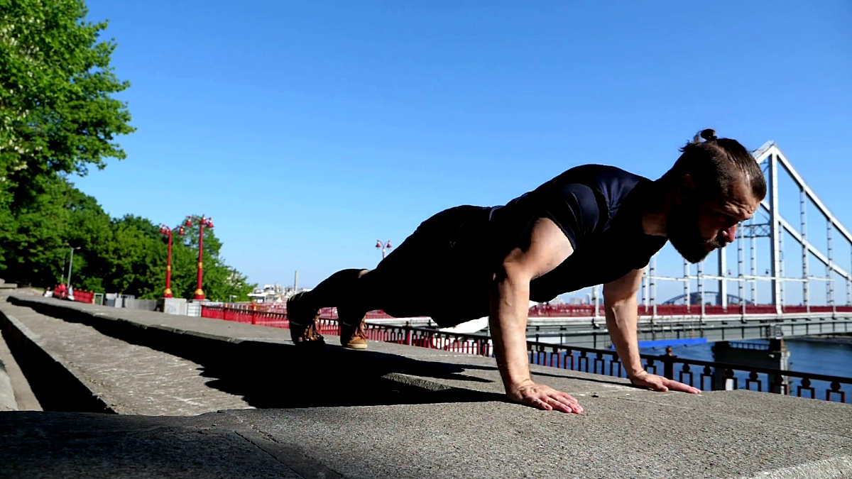 那个长着胡子的男人在桥附近做俯卧撑运动。户外健身训练。