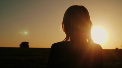 一个深思熟虑的女人看着夕阳，背影。梦想和孤独的概念，向前看