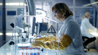 资深女性生物学家在隔离手套箱中处理样品。她在一个现代化的，忙碌的实验室里，配备了最先进的技术。