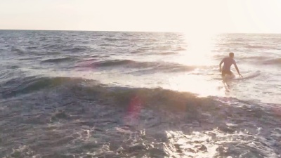 年轻的冲浪者穿着潜水服在日落时分平静的海水中在冲浪板上游泳鸟瞰无人机小推车
