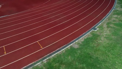 在体育场跑道上，颜色是橙色砖，高角度无人驾驶飞机观看。