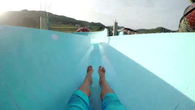 FPV第一人称视图POV 在夏季水上公园的夏日夕阳下，年轻的成年人滑下有趣的滑水滑梯