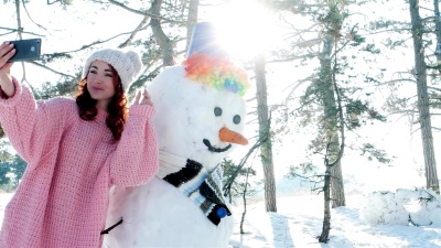 可爱的女孩与雪人合影，冬季自拍，一位年轻女子在冬季森林背光下自拍有趣的手机