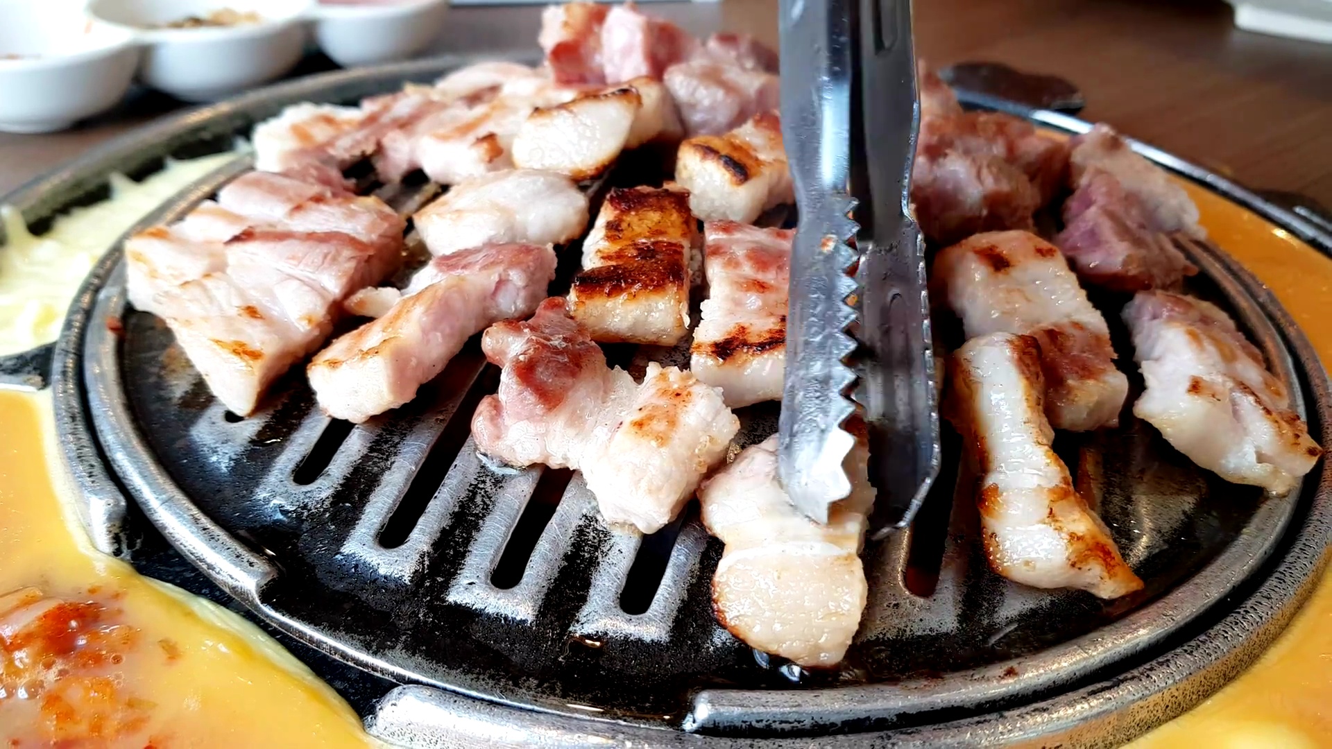 猪肉片烤架和烤盘上的烤肉和烹饪用的大钳子。平底锅的一边有一个煎蛋卷和奶酪。韩国烧烤(BBQ)