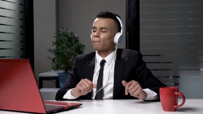 身穿西装的年轻成功的非洲商人戴着耳机在电脑上听音乐，在办公室跳舞。60帧/秒