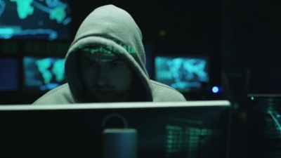 一名男性黑客在电脑上工作，而在黑暗的办公室里，绿色代码字符反映在他的脸上。