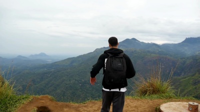 年轻的男性徒步旅行者，背着背包登上山顶，举起双手。一名男子游客站在美丽的峡谷边缘，得意洋洋地伸出双臂。慢动作后视图