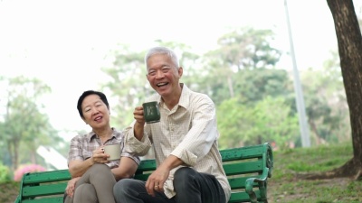 慢动作快乐的亚洲老年夫妇坐在早晨公园喝茶，喝咖啡。交谈和表达爱意