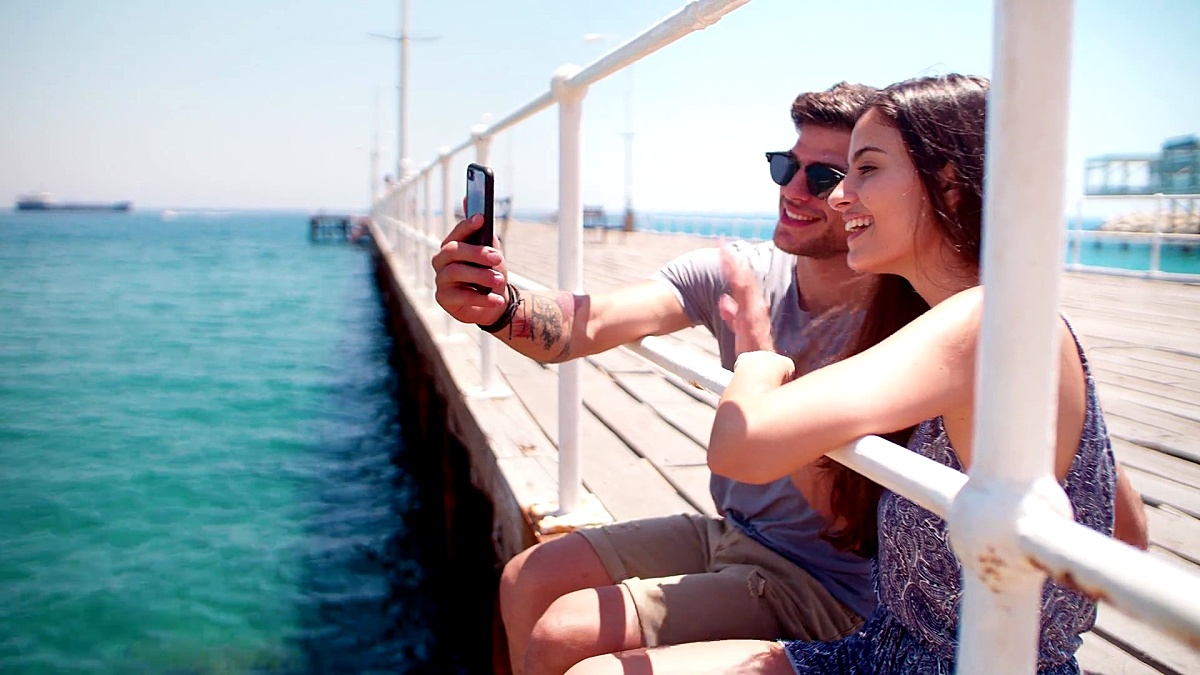 快乐的年轻潮人夫妇在木墩上用智能手机视频聊天